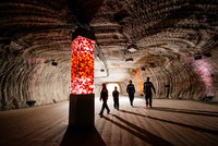 Bildmotiv aus dem Salzbergwerk Berchtesgaden, zu sehen sind eine Lichtsäule aus Salz sowie interessierte Besucher in Overalls