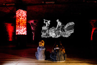 Bildmotiv aus dem Salzbergwerk Berchtesgaden, zu sehen sind eine Lichtsäule aus Salz sowie interessierte Besucher, die eine Videoanimation anschauen